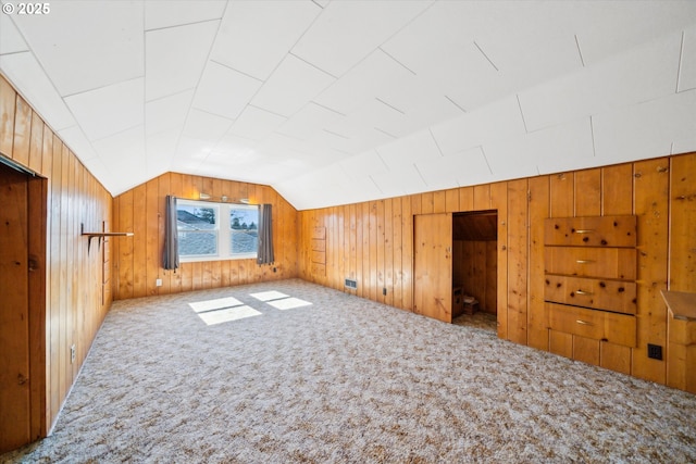 additional living space with vaulted ceiling, wood walls, and carpet