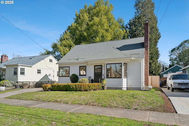 view of front of property with roof with shingles, a front lawn, a chimney, and fence