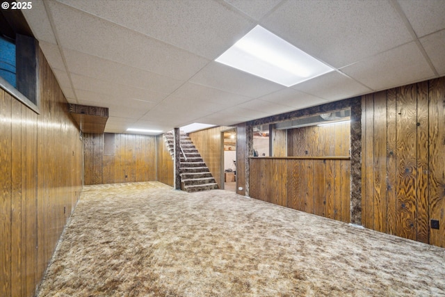 finished below grade area featuring carpet floors, stairway, a drop ceiling, and wooden walls