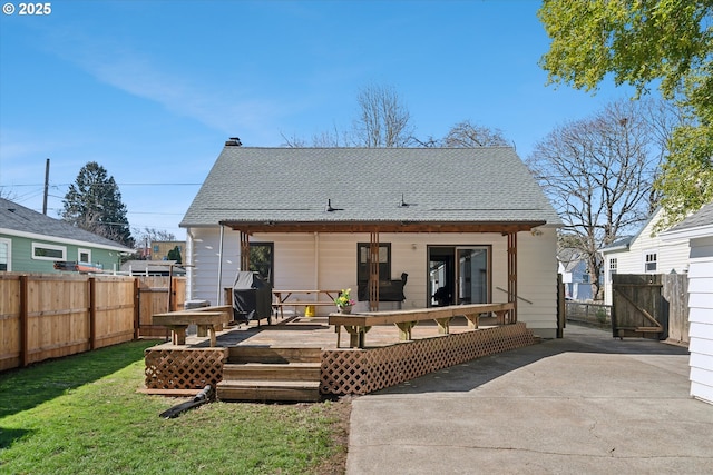 rear view of house featuring a deck, a yard, roof with shingles, and fence