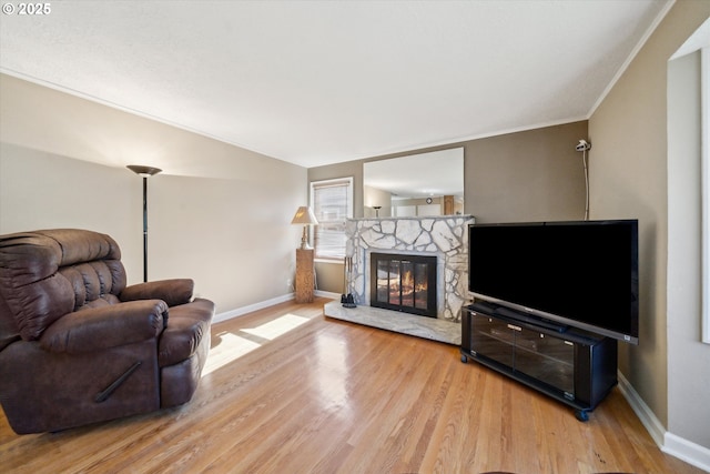 living area with baseboards, wood finished floors, vaulted ceiling, crown molding, and a fireplace