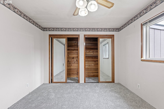 unfurnished bedroom featuring carpet flooring, two closets, and ceiling fan