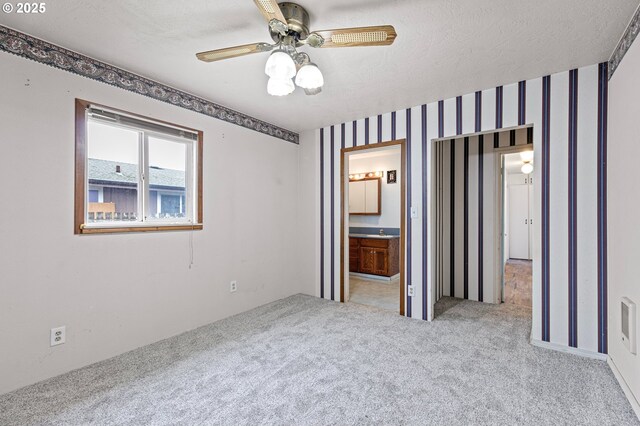 unfurnished bedroom with ceiling fan, light colored carpet, connected bathroom, and a textured ceiling