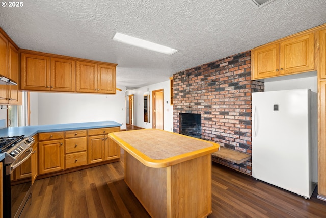 kitchen with freestanding refrigerator, a peninsula, a fireplace, stainless steel range with gas stovetop, and dark wood-style flooring