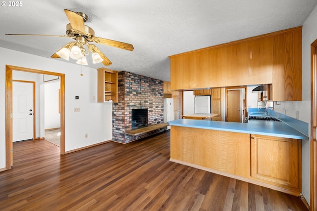 kitchen with brown cabinetry, dark wood finished floors, a peninsula, freestanding refrigerator, and a textured ceiling