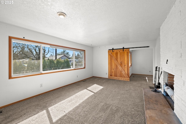 unfurnished living room featuring a barn door, carpet floors, a textured ceiling, and baseboards