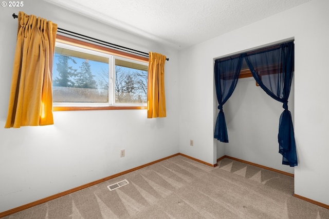 carpeted empty room featuring baseboards, visible vents, and a textured ceiling