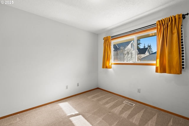 carpeted spare room featuring visible vents, a textured ceiling, and baseboards