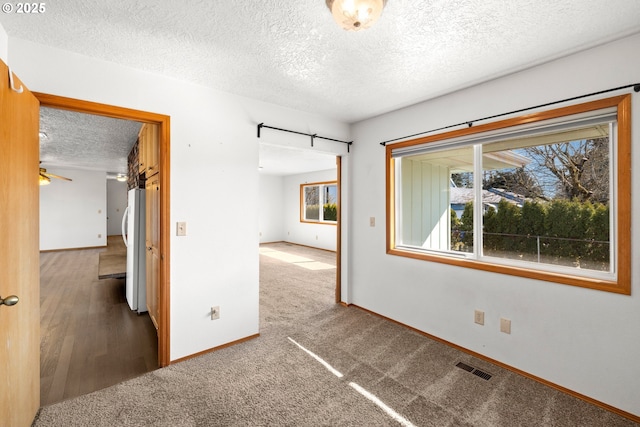 empty room featuring visible vents, a textured ceiling, carpet flooring, baseboards, and ceiling fan