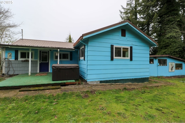 rear view of house with a wooden deck, a lawn, and a hot tub