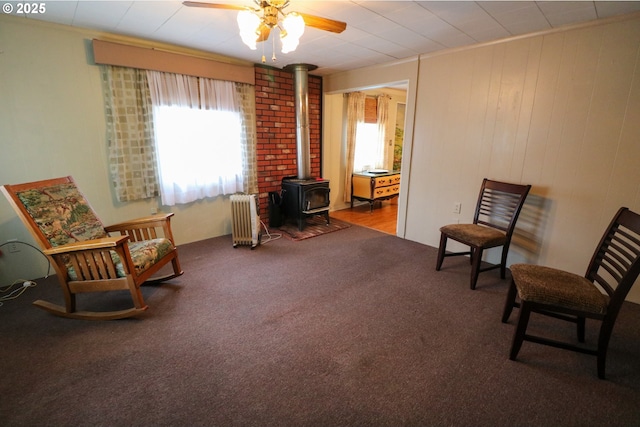 living area featuring carpet floors, radiator, a wood stove, and ceiling fan