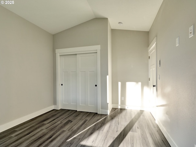 unfurnished bedroom featuring a closet, dark wood-type flooring, and lofted ceiling