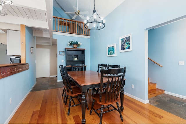 dining space featuring wood-type flooring, ceiling fan with notable chandelier, and high vaulted ceiling