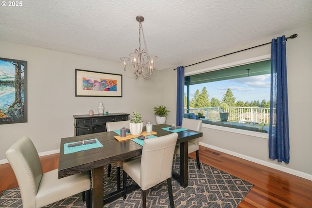 dining space featuring baseboards, visible vents, wood finished floors, a textured ceiling, and a chandelier