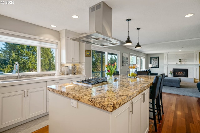 kitchen featuring island exhaust hood, gas cooktop, a sink, wood finished floors, and a glass covered fireplace