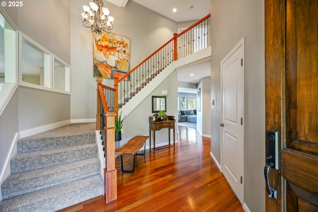 stairway with baseboards, a towering ceiling, wood finished floors, a notable chandelier, and recessed lighting