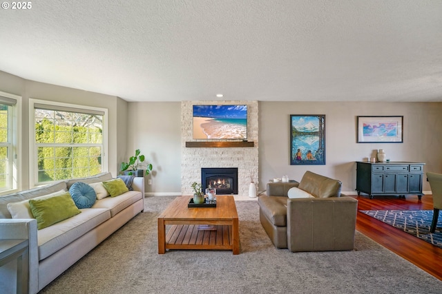 living area with a textured ceiling, a fireplace, wood finished floors, and baseboards