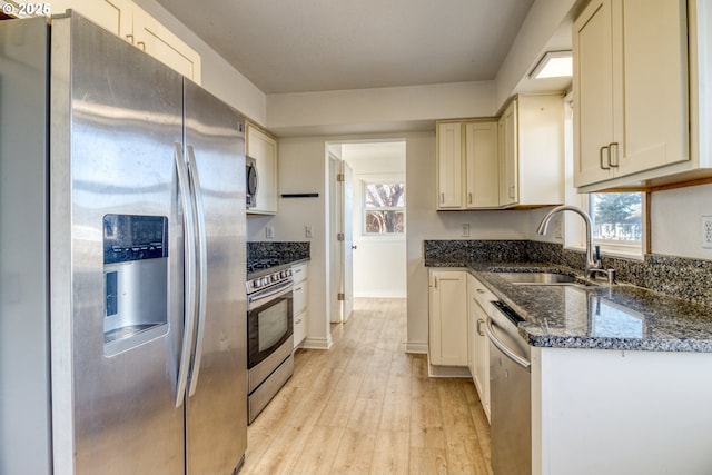 kitchen with a wealth of natural light, sink, dark stone counters, light hardwood / wood-style floors, and stainless steel appliances