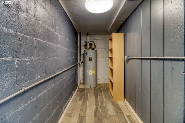 basement featuring light hardwood / wood-style floors, water heater, and a textured ceiling