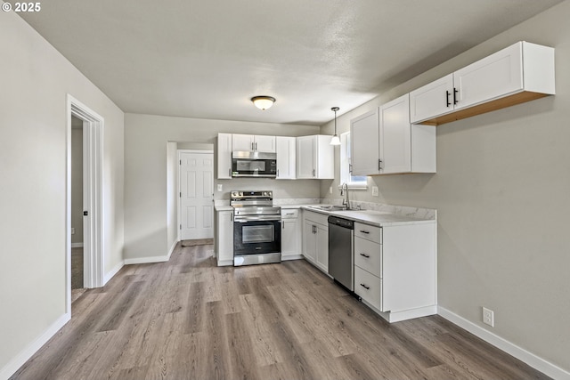 kitchen featuring a sink, stainless steel appliances, light wood finished floors, white cabinets, and baseboards
