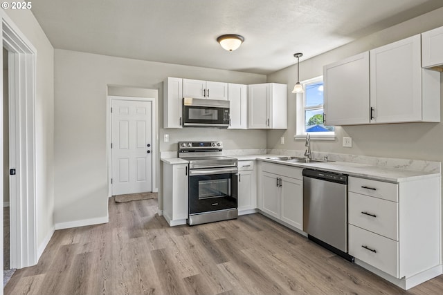 kitchen with light wood finished floors, a sink, stainless steel appliances, white cabinetry, and light countertops