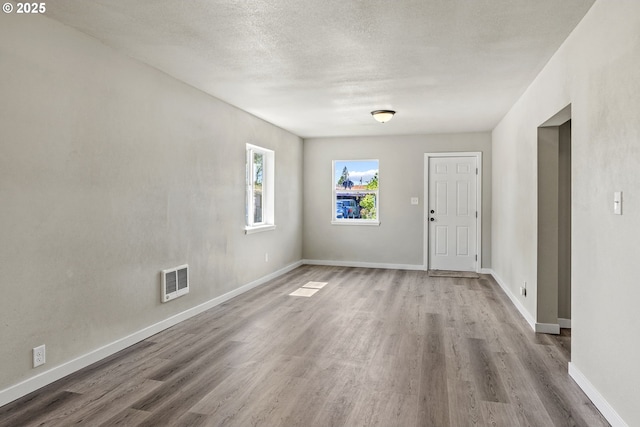 spare room with baseboards, visible vents, a textured ceiling, and wood finished floors