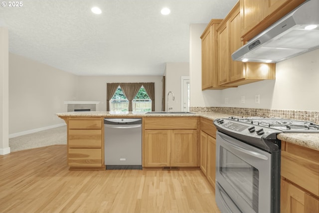 kitchen with open floor plan, a peninsula, stainless steel appliances, under cabinet range hood, and a sink