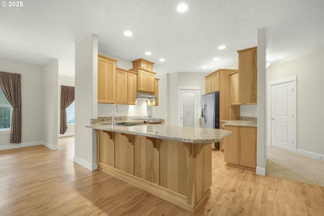 kitchen with under cabinet range hood, a peninsula, light wood-type flooring, a kitchen bar, and stainless steel fridge