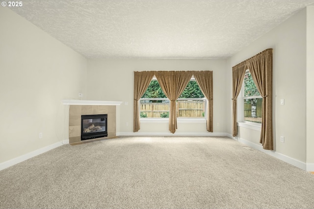 unfurnished living room with a tile fireplace, carpet flooring, a textured ceiling, and baseboards