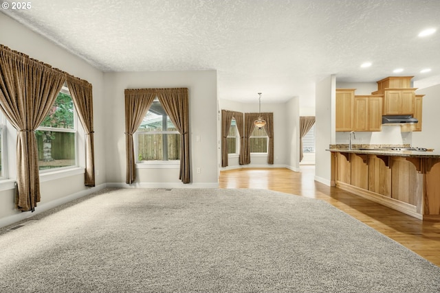 unfurnished living room with a textured ceiling, recessed lighting, a sink, baseboards, and light wood-type flooring