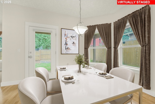 dining space with light wood-style floors, a textured ceiling, and baseboards