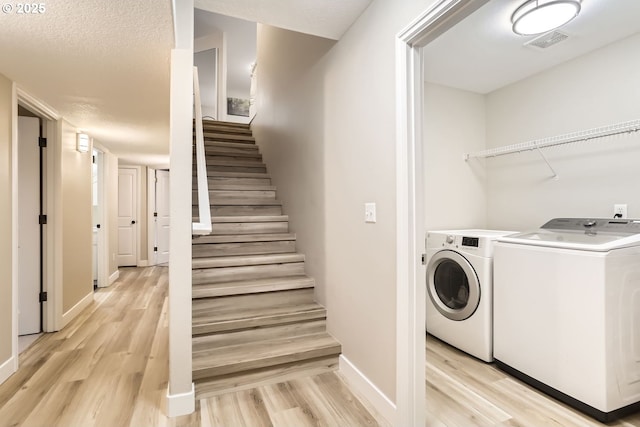 laundry room with light hardwood / wood-style floors, washing machine and dryer, and a textured ceiling