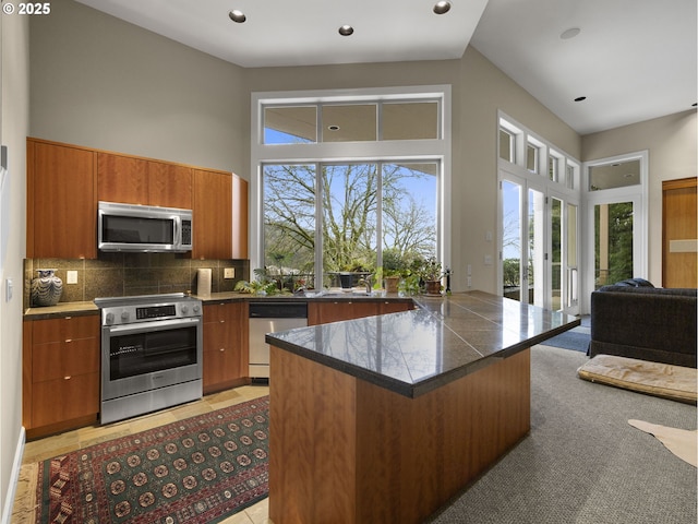 kitchen featuring a high ceiling, appliances with stainless steel finishes, decorative backsplash, a kitchen breakfast bar, and light tile patterned floors