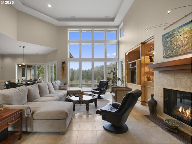 living room with a tile fireplace, a raised ceiling, and a towering ceiling