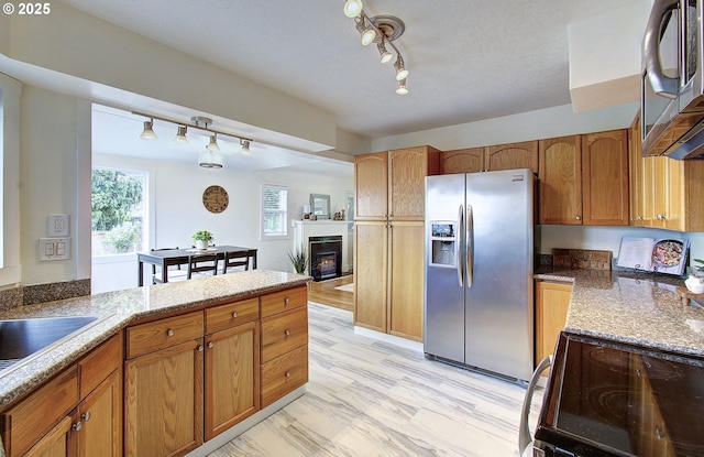 504 NW Fargo St, Camas, WA 98607 - kitchen featuring appliances with stainless steel finishes, rail lighting, a warm lit fireplace, brown cabinets, and a peninsula