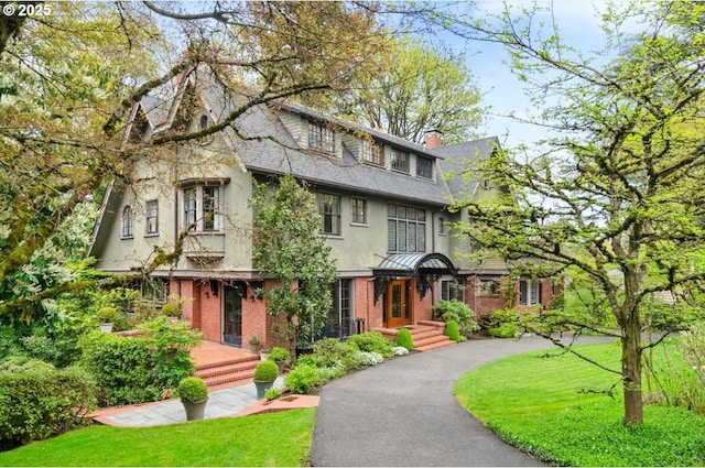 view of front of house featuring a chimney, aphalt driveway, stucco siding, brick siding, and a front lawn