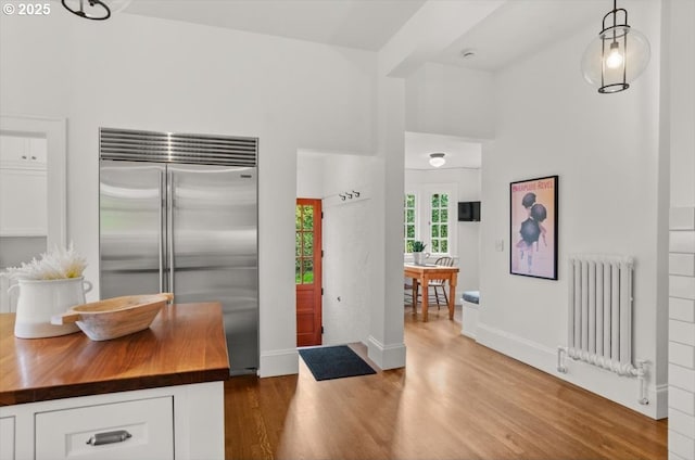 1965 SW Montgomery Pl, Portland, OR 97201 - kitchen featuring radiator heating unit, stainless steel built in refrigerator, butcher block countertops, wood finished floors, and white cabinetry