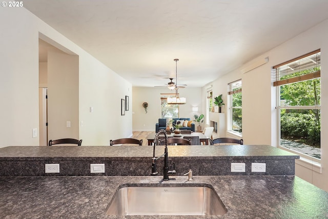 kitchen featuring a ceiling fan, open floor plan, dark stone counters, and a sink