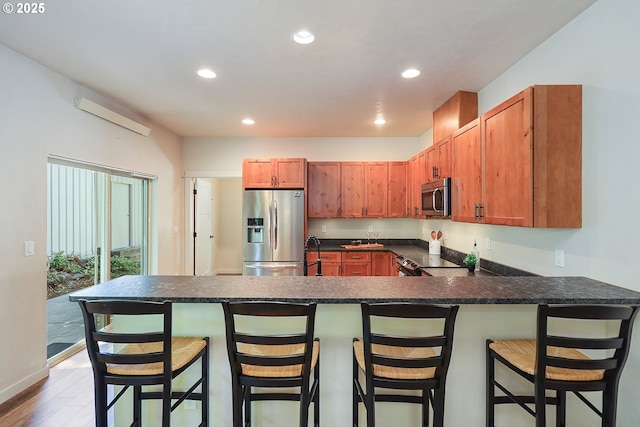 kitchen with recessed lighting, a sink, a peninsula, dark countertops, and stainless steel appliances
