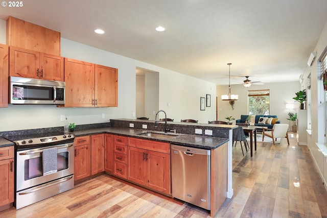 kitchen with decorative light fixtures, a sink, a peninsula, light wood-style floors, and appliances with stainless steel finishes