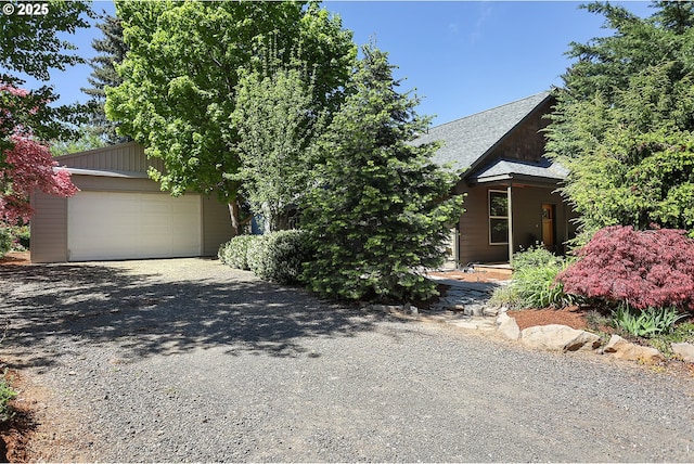 view of property hidden behind natural elements with gravel driveway, a shingled roof, and a garage