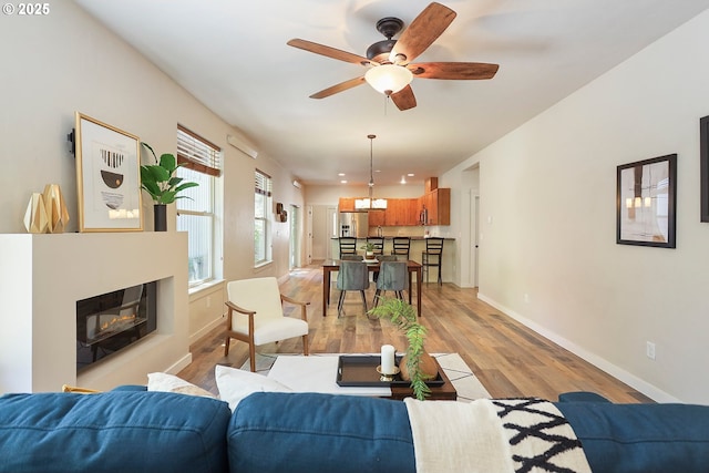 living room with ceiling fan, light wood-style flooring, baseboards, and a glass covered fireplace