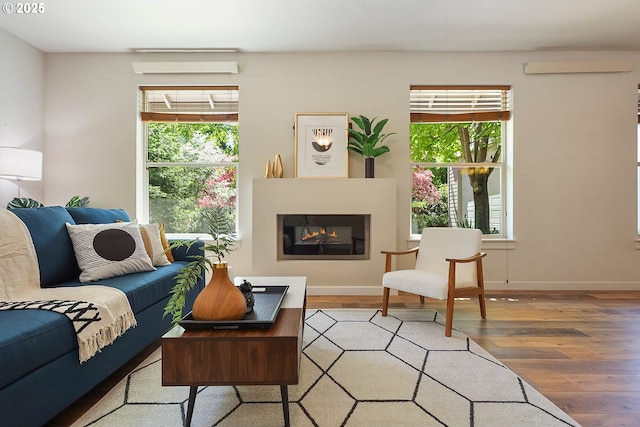 living room with baseboards, light wood-style floors, a glass covered fireplace, and plenty of natural light