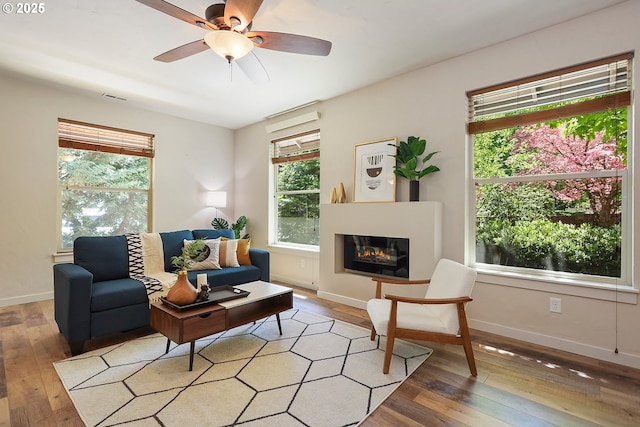 living room featuring light wood finished floors, a glass covered fireplace, plenty of natural light, and baseboards