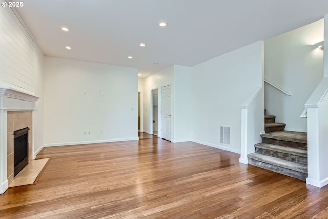 unfurnished living room with stairs, recessed lighting, visible vents, light wood-type flooring, and a tile fireplace