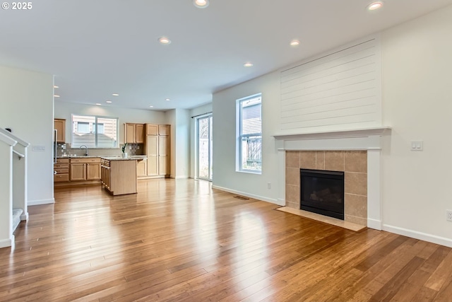 unfurnished living room with light wood-type flooring, recessed lighting, baseboards, and a tile fireplace