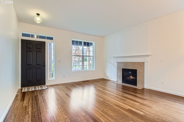 foyer entrance with a tile fireplace, wood finished floors, visible vents, and baseboards