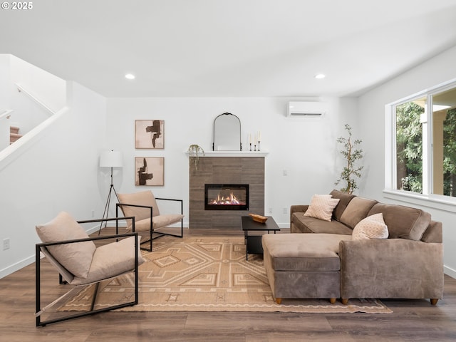 living room with a tile fireplace, an AC wall unit, and wood-type flooring