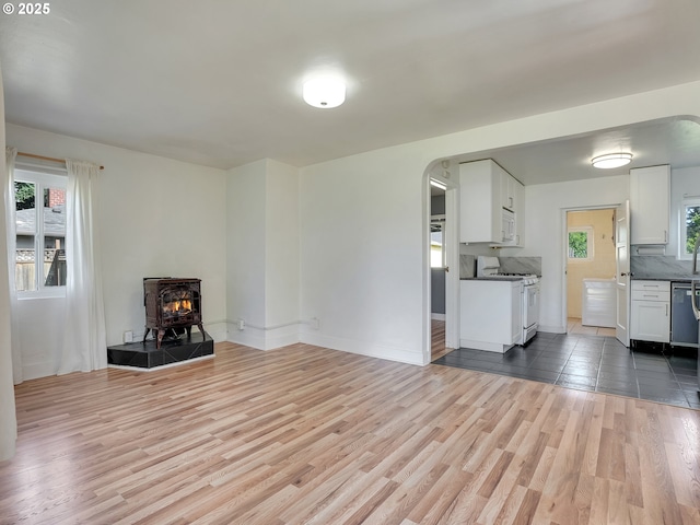 12226 SE Raymond St, Portland, OR 97236 - unfurnished living room with arched walkways, a wood stove, light wood finished floors, and baseboards