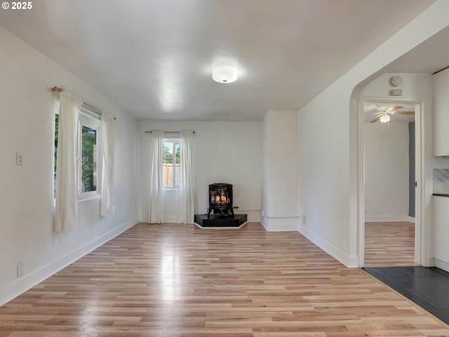 12226 SE Raymond St, Portland, OR 97236 - unfurnished living room featuring a wood stove, light wood finished floors, arched walkways, and baseboards